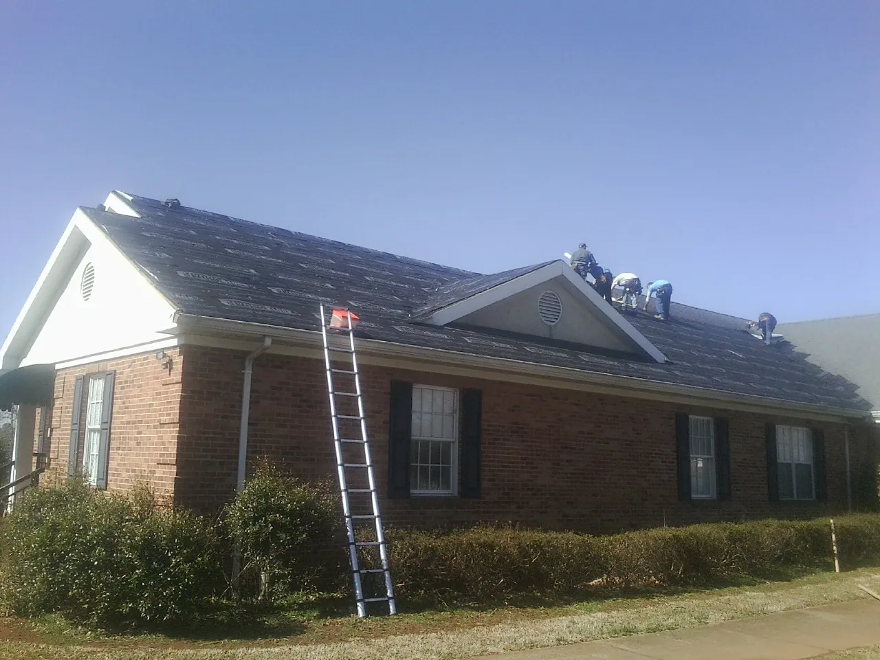 Crew tearing shingles off a brick ranch roof with a ladder set — Emergency Roof Repair work by our crew in Chesterfield