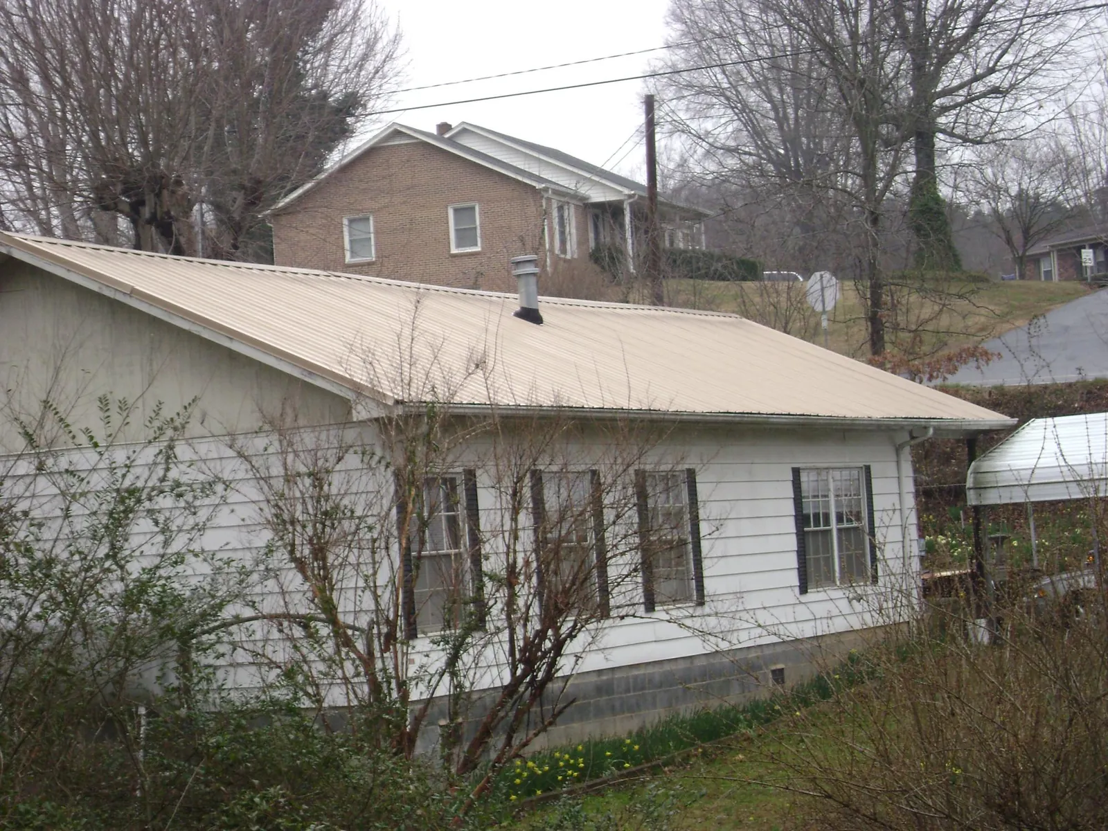 Tan metal roof on a white sided house set into a hillside — Commercial Roofing by Roofing Brothers in Chesterfield